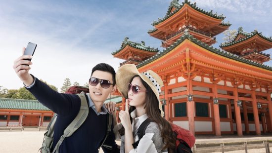 A young and fashionable Asian couple taking a selfie in front of the Heian Shrine, Kyoto, Japan.